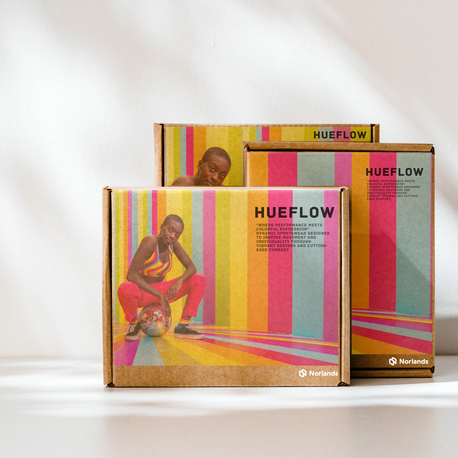 The image showcases custom boxes designed for HueFlow, a vibrant sportswear brand that blends performance with individuality. Featuring bold rainbow-striped designs and a model in colorful activewear, the packaging reflects the brand's dynamic identity. These custom printed boxes, crafted by Norlands Custom Packaging Vancouver, highlight creativity, sustainability, and premium quality, perfectly aligning with HueFlow's mission of vibrant aesthetics and cutting-edge comfort.