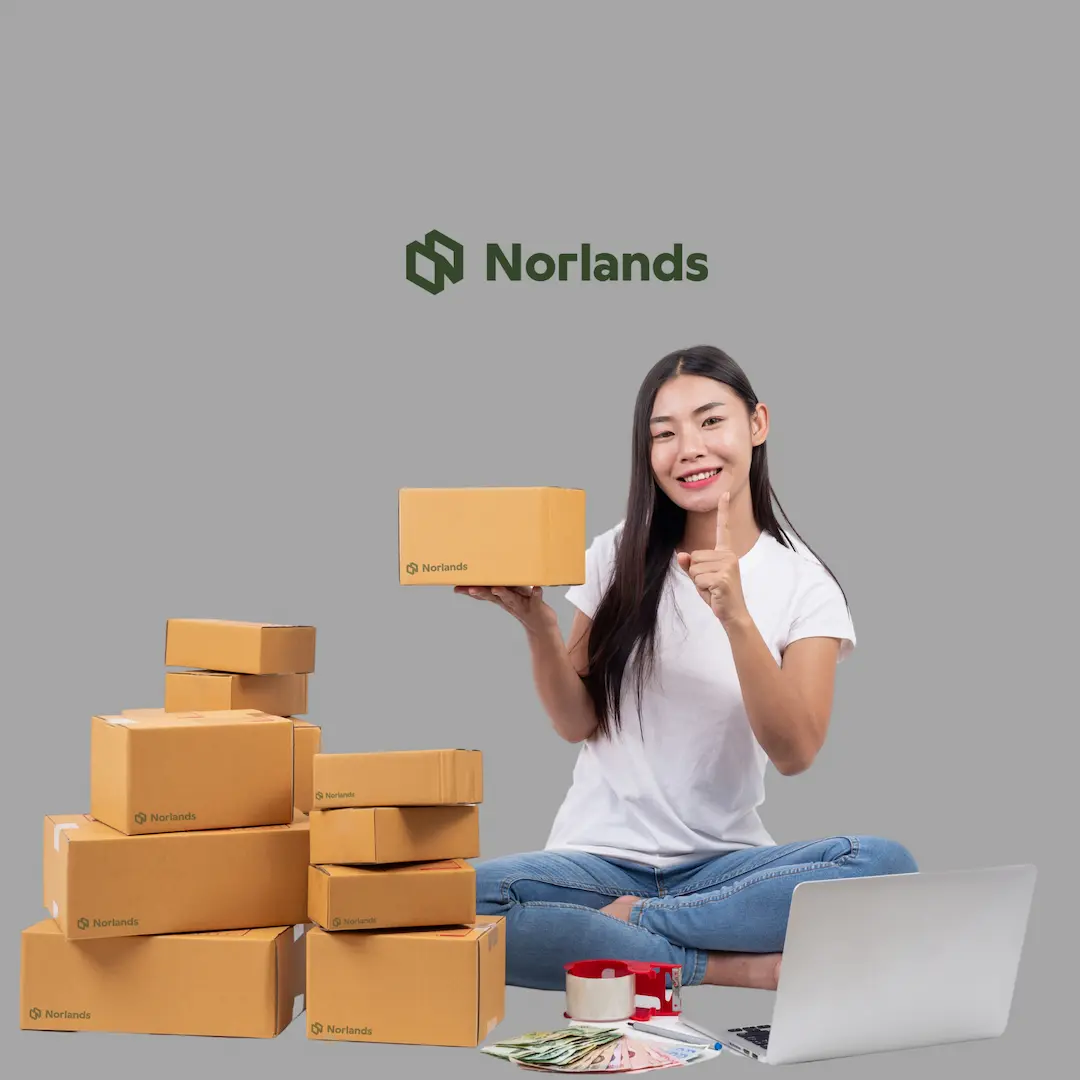 Smiling woman sitting cross-legged with a laptop, holding a Norlands-branded cardboard box, surrounded by multiple packages—representing small business shipping and eco-friendly packaging solutions.