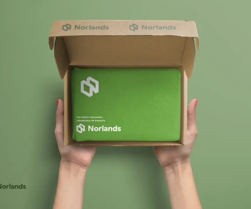 Custom Packaging in Vancouver.Hands holding an open Norlands cardboard box with a neatly wrapped green package inside, showcasing eco-friendly, branded packaging with a premium feel.