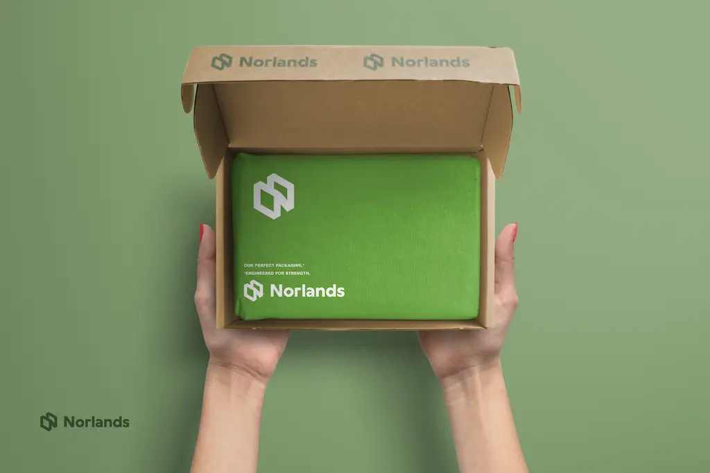 Custom Packaging in Vancouver.Hands holding an open Norlands cardboard box with a neatly wrapped green package inside, showcasing eco-friendly, branded packaging with a premium feel.