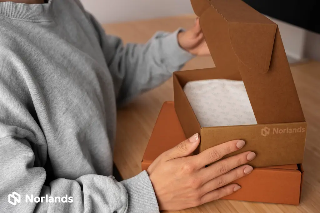 Close-up of a person opening a brown corrugated cardboard box with custom printed tissue paper inside, showcasing eco-friendly packaging by Norlands.