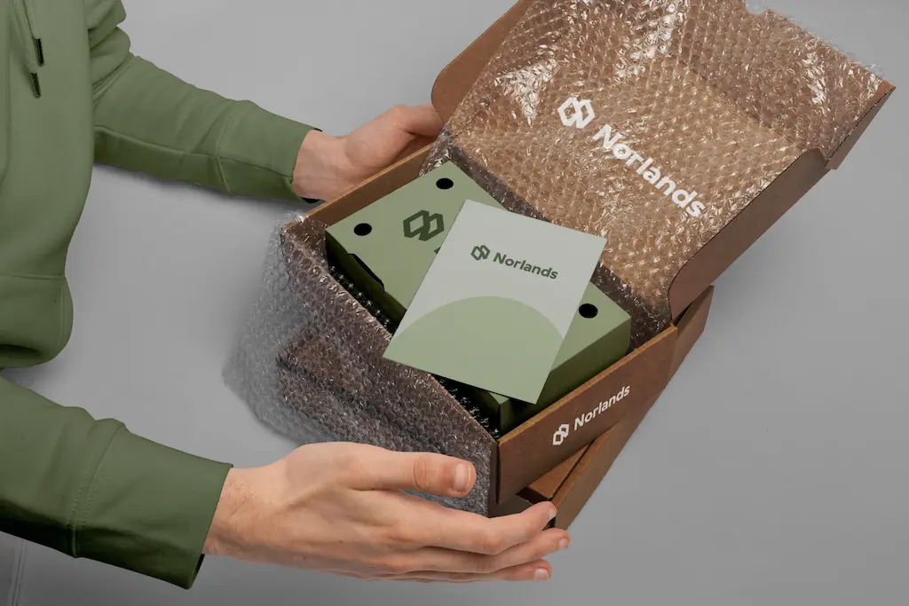 A person opens a Norlands branded cardboard box lined with bubble wrap, revealing neatly packed items and an insert card.