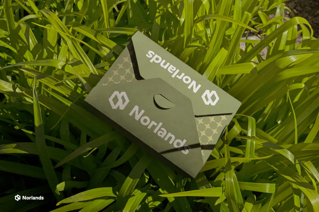 A green Norlands branded cardboard box placed on fresh green grass, highlighting eco-friendly packaging.