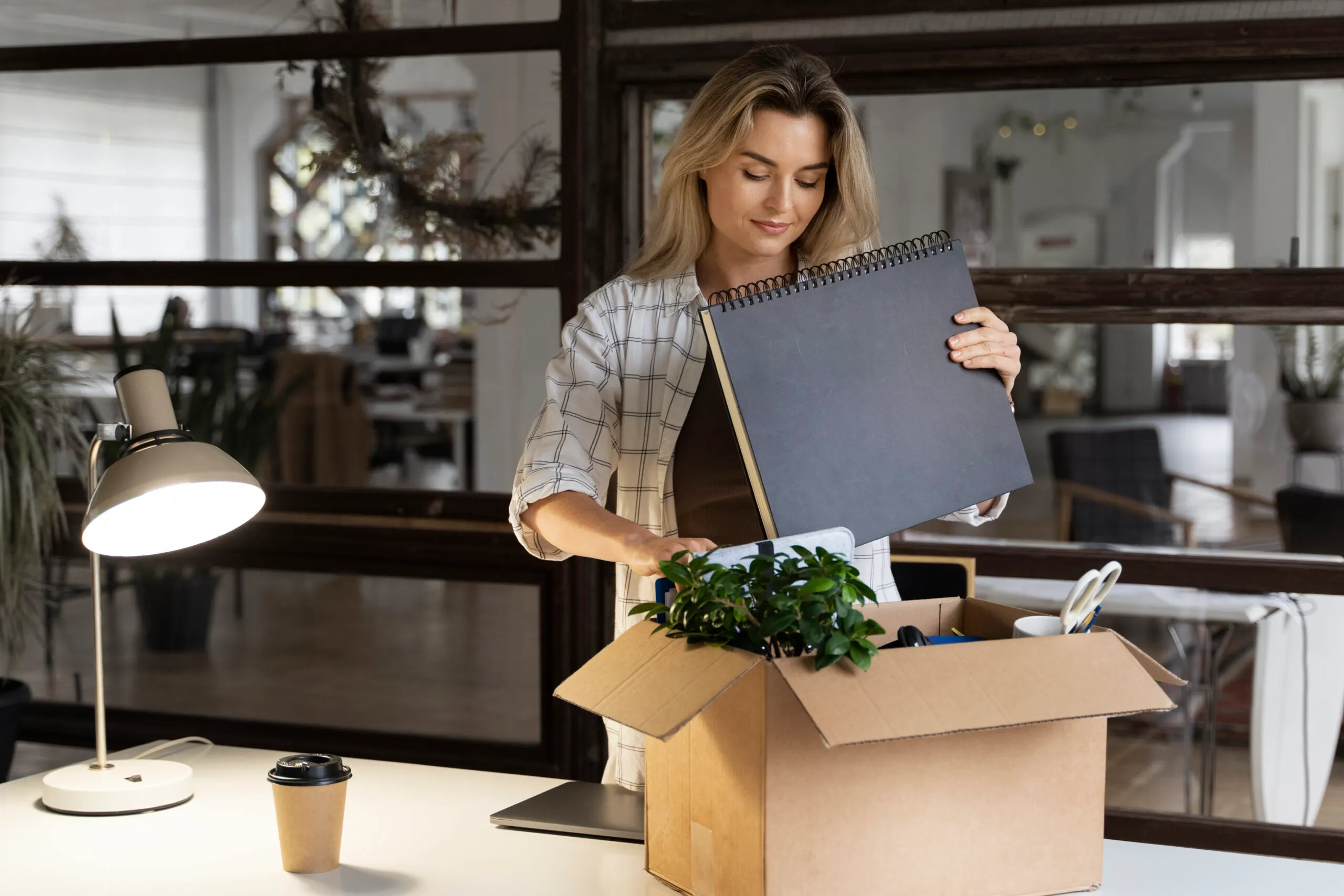 Person unpacking a cardboard Norlands box in a modern office, placing a notebook and plant on the desk, symbolizing organized moving and eco-friendly packaging.