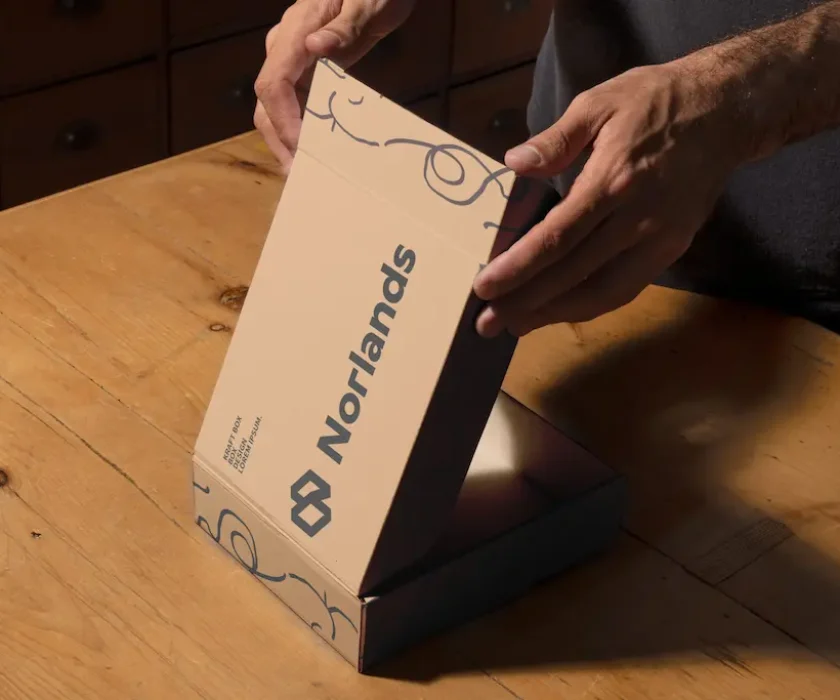box manufacturers in Vancouver-Hands opening a custom Norlands packaging box made of eco-friendly cardboard on a wooden table.