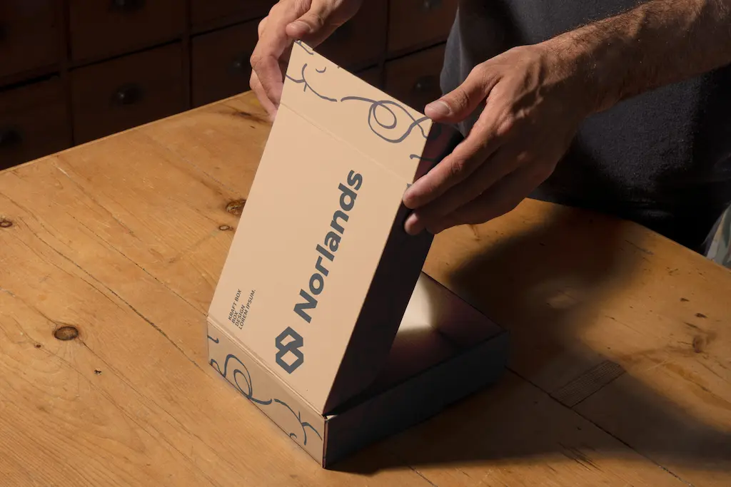 box manufacturers in Vancouver-Hands opening a custom Norlands packaging box made of eco-friendly cardboard on a wooden table.