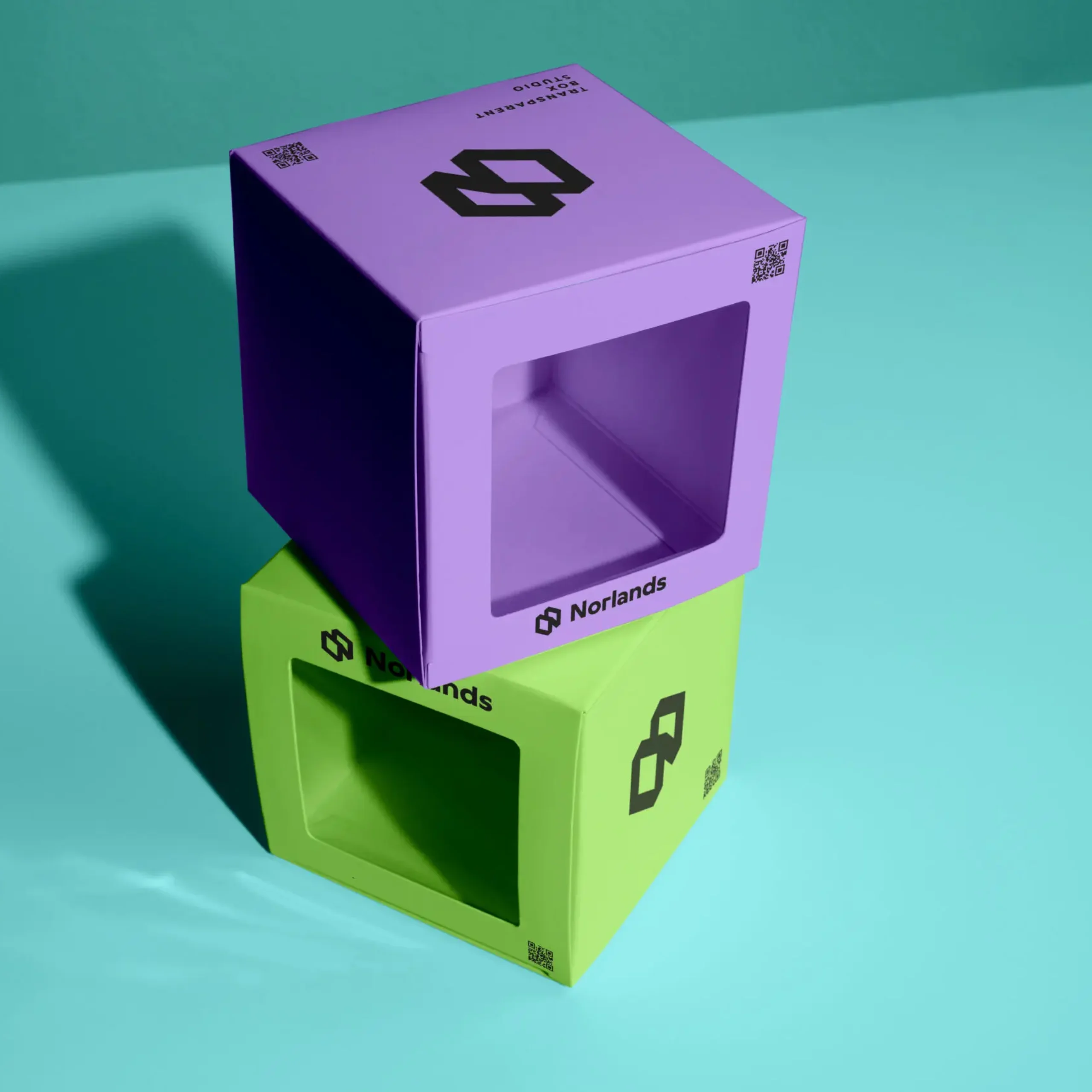 Two modern Norlands packaging boxes in bright purple and green with transparent display windows, stacked on a turquoise surface under studio lighting.