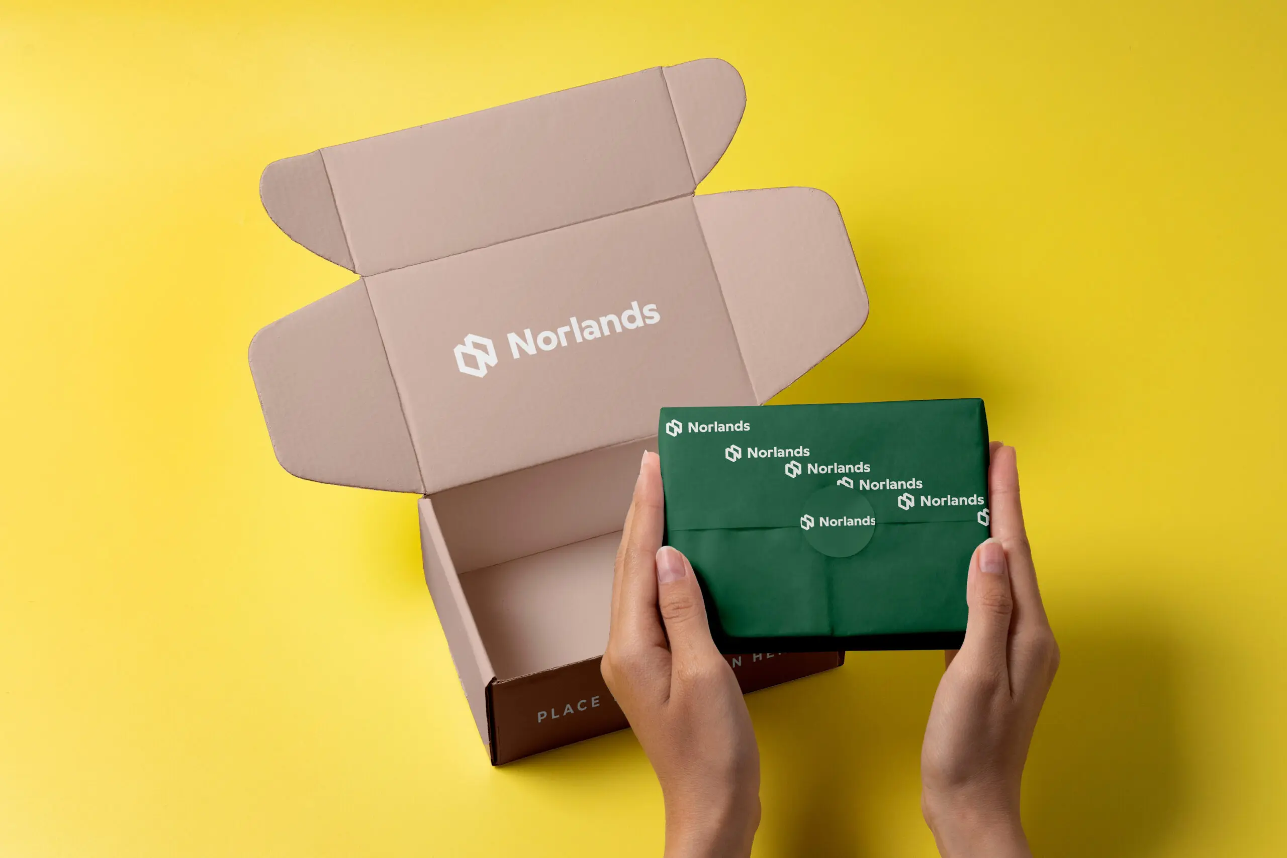 Hands holding a green Norlands-branded package beside an open custom shipping box with Norlands logo, displayed on a vibrant yellow background.