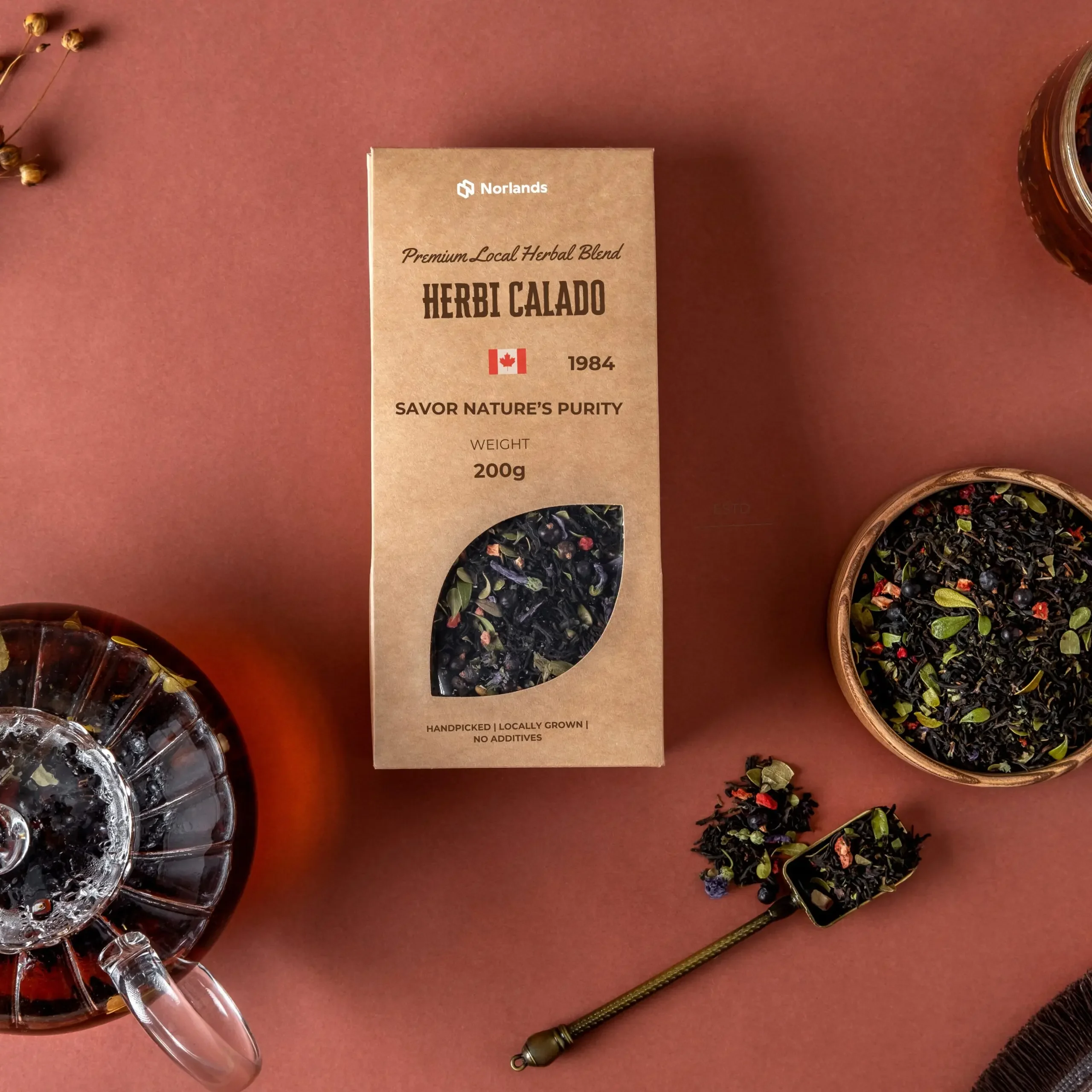 Custom Product Packaging in Canada.Kraft paper tea packaging box labeled “Herbi Calado” with loose herbal tea, spoon, and glass teapot arranged on a brown background.