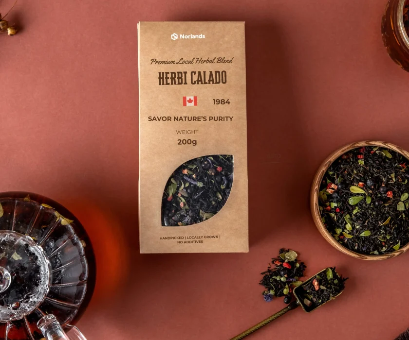 Custom Product Packaging in Canada.Kraft paper tea packaging box labeled “Herbi Calado” with loose herbal tea, spoon, and glass teapot arranged on a brown background.