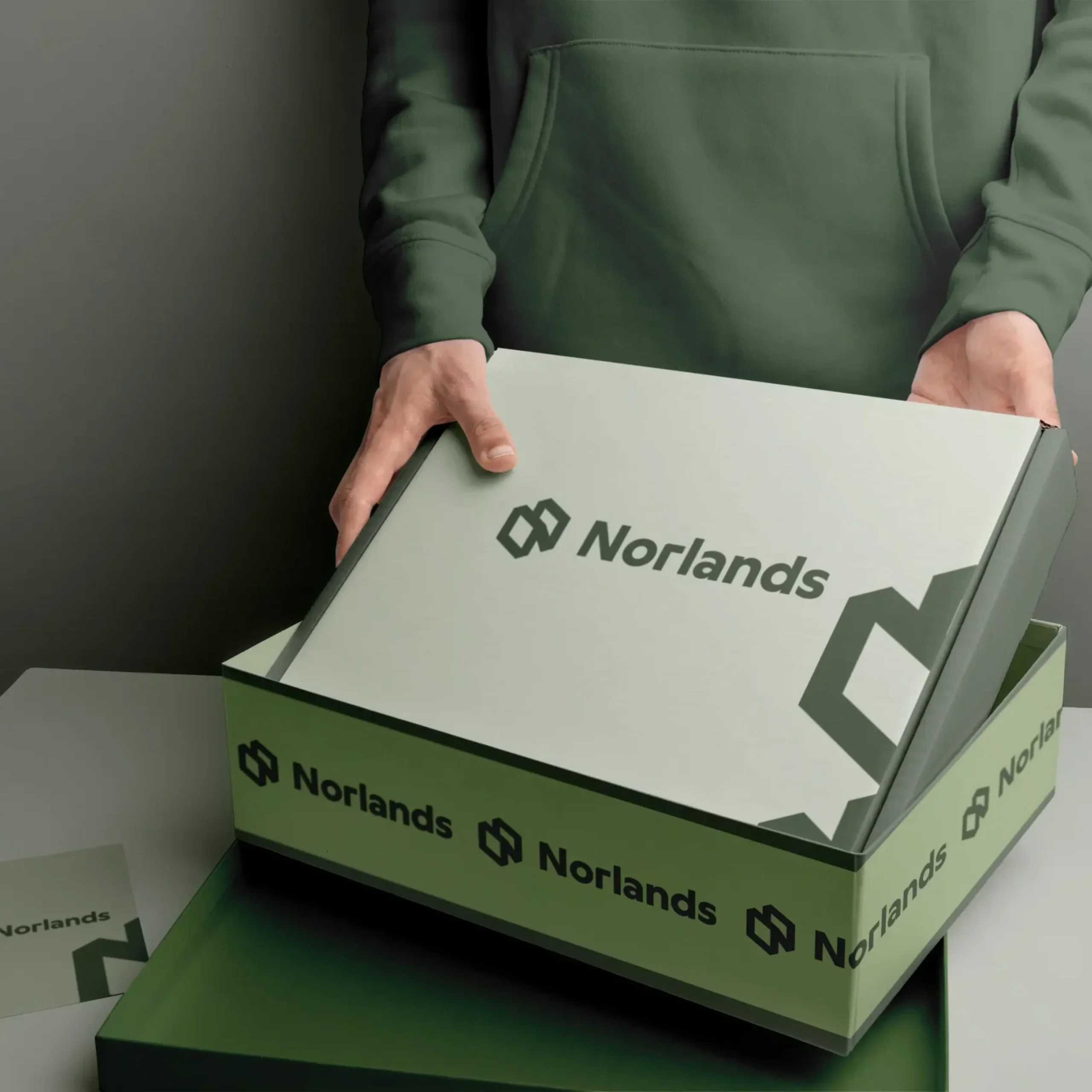 custom boxes in Canada A person in a green hoodie opens a sleek green NORLANDS box with a modern logo design in a softly lit setting.