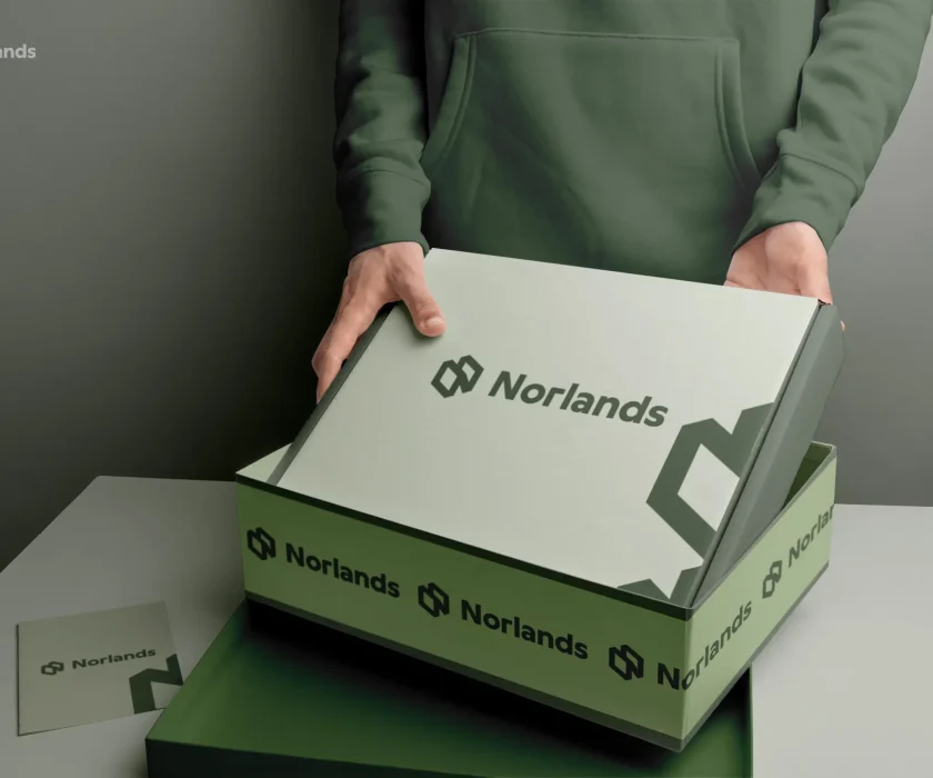 custom boxes in Canada A person in a green hoodie opens a sleek green NORLANDS box with a modern logo design in a softly lit setting.