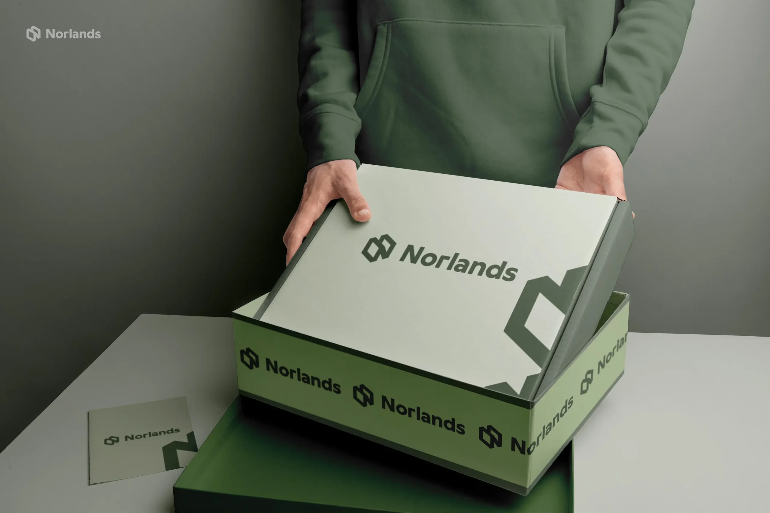 custom boxes in Canada A person in a green hoodie opens a sleek green NORLANDS box with a modern logo design in a softly lit setting.